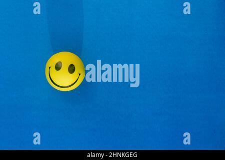 Expression anthropomorphique de visage smiley d'un Squeeze ball ou stress ball isolé sur fond bleu. Vue du dessus de la table. Gros plan. Arrière-plan sourire heureux Banque D'Images