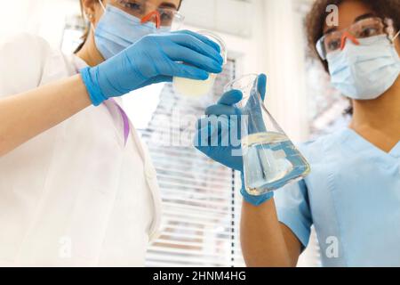 Laboratoire de test COVID-19. Deux femmes scientifiques de laboratoire médical collègues portant des masques de visage travaillant avec des tubes à essai, multi-ethnique étudiants diplômés Banque D'Images