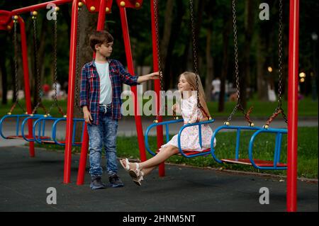La date romantique des enfants dans le parc d'été, l'amitié, le premier amour. Garçon et fille sur des balançoires. Enfants s'amuser à l'extérieur, bonne enfance Banque D'Images