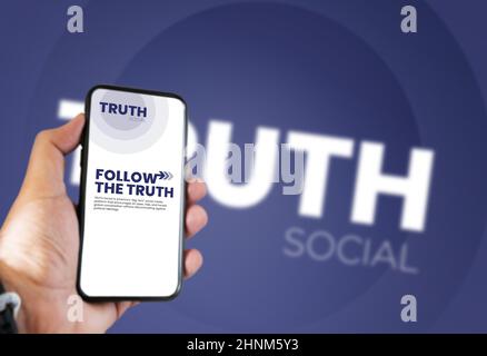 Main tenant un téléphone avec l'application mobile Truth social à l'écran et le logo flou en arrière-plan Banque D'Images