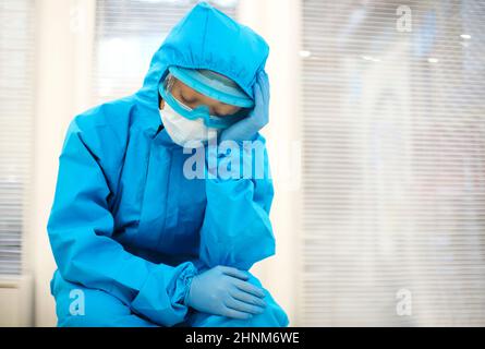 Femme fatiguée médecin dans l'équipement de protection individuelle EPI se sentant déprimé après un déplacement stressant difficile pendant la pandémie Covid-19, assis sur le sol Banque D'Images