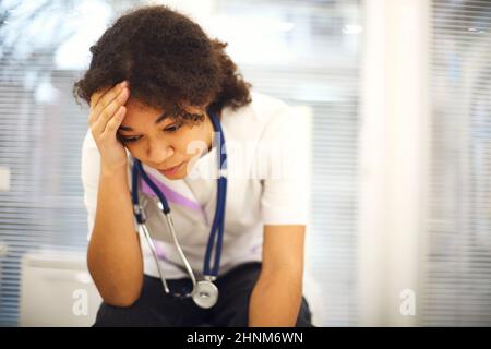 Triste déprimé jeune afro-américaine infirmière assis avec l'expression du visage frustré, se sentant submergé par la charge de travail dans la clinique, ethnique femme médecin fe Banque D'Images