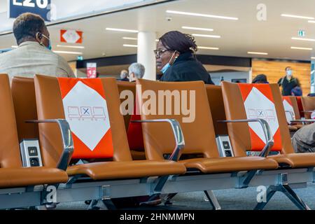 Charles de Gaulle, Paris, le 13 janvier 2022 - Noir homme et femme en conversation derrière des sièges vides avec des signes sociaux de distanciation à l'aéroport Banque D'Images