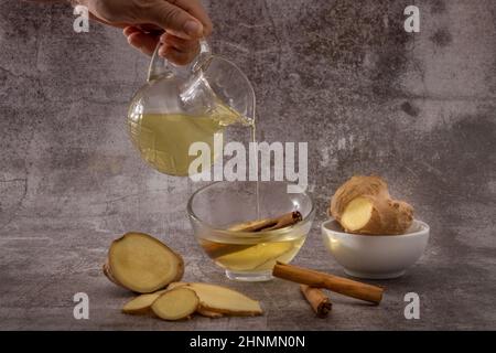 préparation d'une infusion de gingembre et de cannelle avec des racines naturelles de produits frais et un bâton de cannelle servi dans un pichet et une tasse Banque D'Images