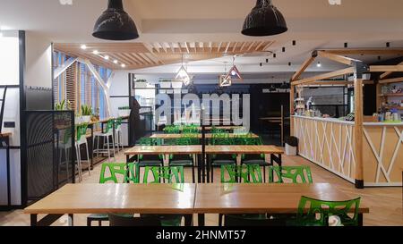 Cafétéria, pas de personnes salle à manger avec des tables en bois et des chaises vertes. Intérieur avec éléments en bois et en métal. Salle à manger moderne avec éclairage par fenêtre. Ukraine, Kiev - 19 février 2021 Banque D'Images