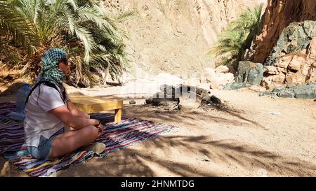 fille assise sur le tapis arabe en position de yoga lotus. Jeune touriste se reposant dans le désert, se cachant à l'ombre d'un palmier lors d'une chaude journée ensoleillée lors d'une excursion dans un canyon en Egypte. Banque D'Images