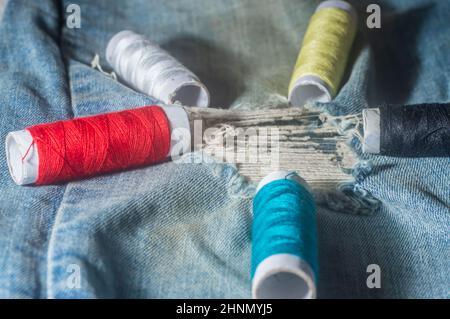 Bobines avec fils de couture colorés avec jeans en arrière-plan, concept de couture, espace de copie dans des parties de l'image. Banque D'Images