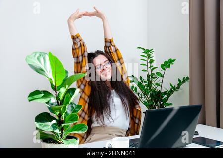 Femme souriante dans des lunettes s'étendant sur un lieu de travail. Femme travaillant à la maison en utilisant un ordinateur portable assis dans le salon Banque D'Images