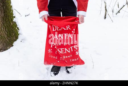 Un homme habillé comme le Père Noël tient un grand sac rouge avec des cadeaux pour les enfants. Banque D'Images