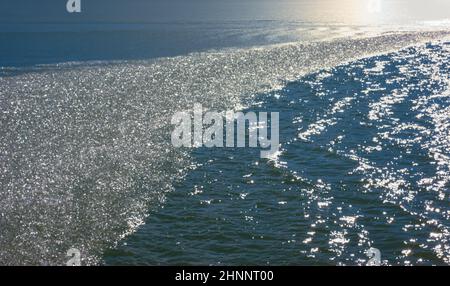 Une banque de cristaux de glace flottant au-dessus d'un corps d'eau ondulée avec la lumière du soleil au loin. Banque D'Images