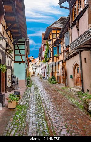 Petite route pittoresque avec maisons à colombages dans le village historique d'Eguisheim en Alsace Banque D'Images