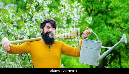 Jardinier barbu avec arrosoir et bêche se préparant à la plantation. Agriculteur travaillant dans le jardin de printemps. Banque D'Images