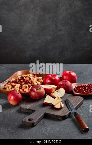 Salade de fruits de baies de vache et de pommes rouges. Encore la vie avec des pommes sur la planche à découper noire, des mûres de lingonyres et de la salade de fruits frais dans un bol en bois Banque D'Images