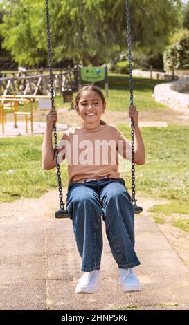 Bonne fille d'enfant s'amuser avec balançoire à chaîne sur le terrain de jeu dans un parc Banque D'Images