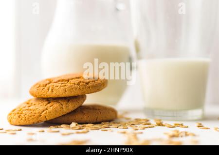 Empilez les biscuits aux flocons d'avoine et les flocons de céréales d'avoine sur une table blanche sur fond de pot à lait en verre Banque D'Images