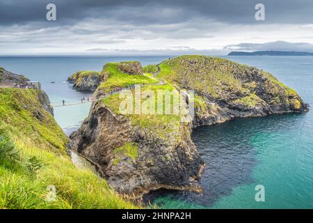 Personnes sur le pont de corde de Carrick a Rede et île pittoresque entourée par l'océan Atlantique turquoise Banque D'Images