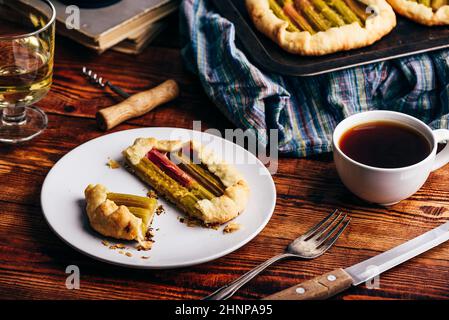 Mini-galette en tranches de rhubarbe sur une assiette blanche avec un verre de vin blanc et une tasse de café Banque D'Images