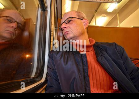 Un homme âgé en lunettes se déplaçant au travail. Homme d'âge moyen regardant par la fenêtre du train. Passager en train express à grande vitesse en Europe. Un homme âgé voyageant en train la nuit Banque D'Images