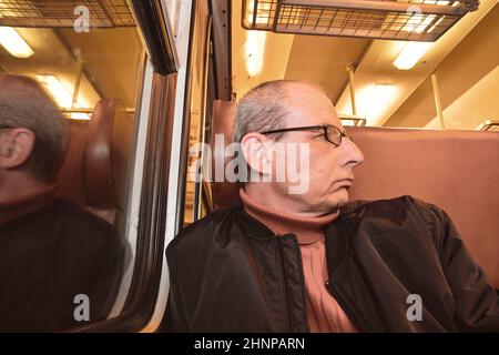 Un homme âgé en lunettes se déplaçant au travail. Homme d'âge moyen regardant par la fenêtre du train. Passager en train express à grande vitesse en Europe. Un homme âgé voyageant en train la nuit Banque D'Images