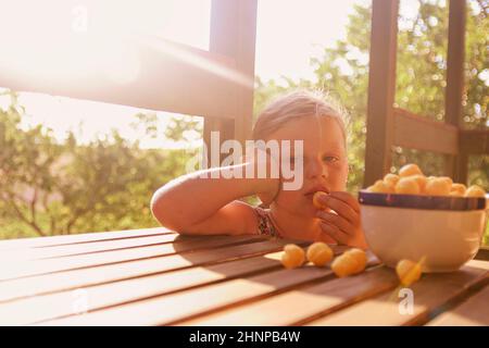 Petite fille est assise sur le porche en été. Boules de fromage dans un bol. Casse-croûte au fromage sur une table. Image romantique et rêveuse. L'été et l'enfance heureuse concept Banque D'Images