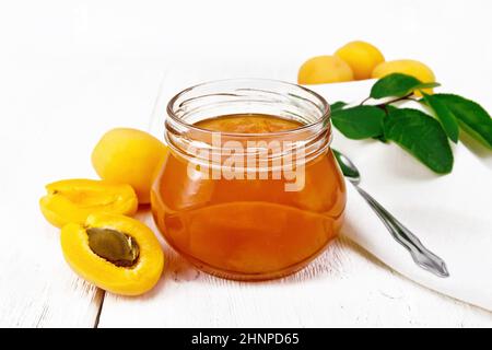 Confiture d'abricot dans un pot en verre, fruits, branche avec feuilles, serviette et cuillère sur fond de bois clair Banque D'Images