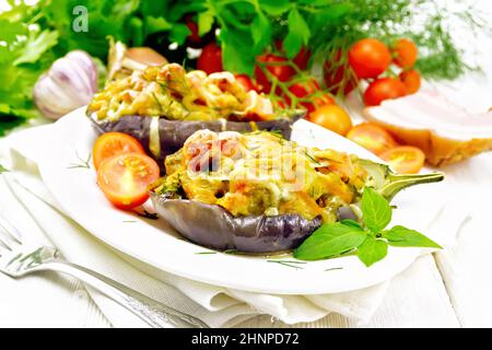 Aubergine farcie au fromage fumé, tomates, oignons, carottes à l'ail, fromage et herbes dans une assiette ovale sur une serviette de cuisine sur un sanglier blanc en bois Banque D'Images