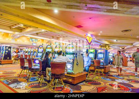 Joueurs assis à l'intérieur du casino jouant avec des machines à sous Banque D'Images