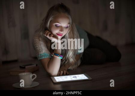 portrait de belle jeune femme blonde regarde et lit sur une tablette et boire du café la nuit. fille utilise la tablette Banque D'Images