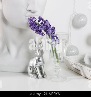 Figurines en céramique de lapins de Pâques de différentes tailles sur la table. Jacinthes bleu et blanc dans des tasses en verre sur fond blanc. Motif Pâques Banque D'Images