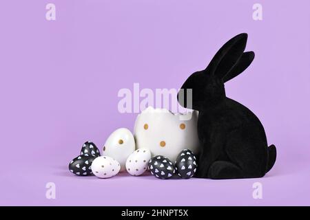 Œufs de pâques noirs et blancs avec des points à côté du lapin sur fond violet Banque D'Images