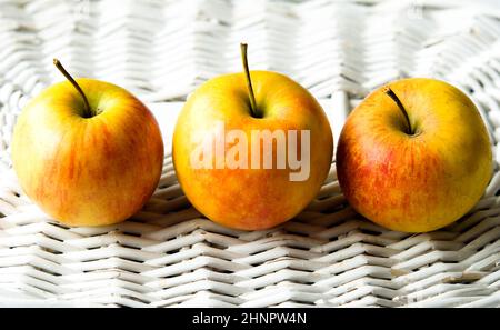 Trois pommes fraîches disposées sur un vieux panier blanc Banque D'Images