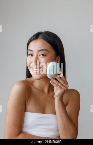 Jeune femme joyeuse utilisant un masseur pour le visage en studio Banque D'Images