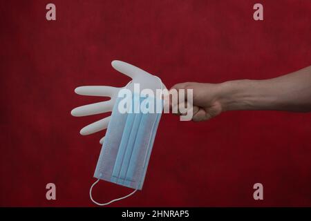 Masque médical suspendu sur gant gonflé. Main tient gant chirurgical blanc avec masque de protection. Fond rouge Banque D'Images