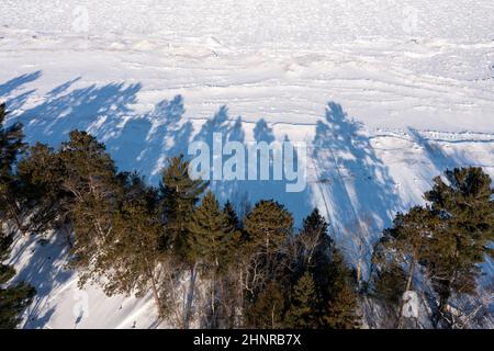 Au train, Michigan - des arbres sur la rive du lac supérieur jettent des ombres sur le lac gelé et recouvert de neige. Banque D'Images