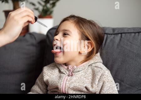 Portrait d'une jeune fille d'âge préscolaire de race blanche prenant des vitamines avec des gouttes à la maison. Concept d'immunité Banque D'Images