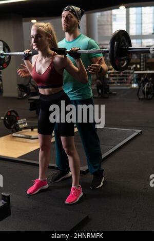 L'entraînement dirigé par un instructeur aide un beau client à effectuer des exercices dans un club de remise en forme, le concept de jouer du sport avec un loisir professionnel de gym Banque D'Images