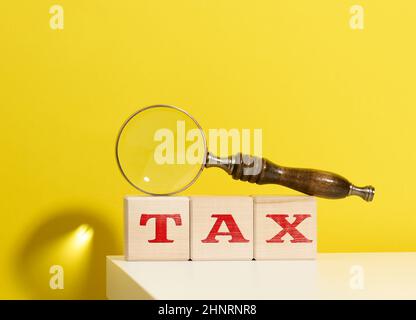 cubes en bois avec la taxe d'inscription et une loupe marron sur fond jaune Banque D'Images