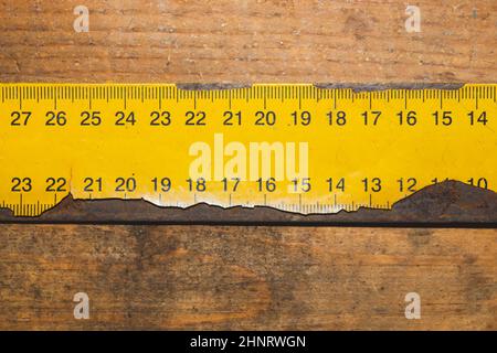 Ancienne règle jaune rouillée avec numéros noirs sur une table en bois en état de marche. Arrière-plan industriel. Atelier de menuiserie avec espace de copie Banque D'Images