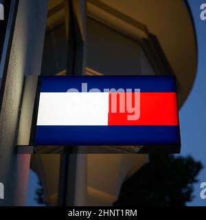 Néon avec le logo du designer de mode Tommy Hilfiger dans une rue commerçante à Berlin dans la soirée Banque D'Images