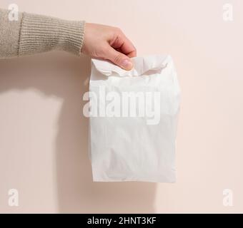 la main femelle tient un sac de papier complet sur un fond beige.Refus d'emballage en plastique, livraison de nourriture Banque D'Images