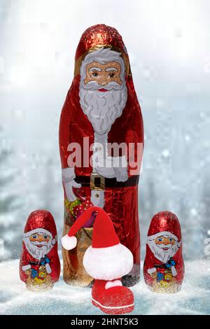 Gros plan de divers joyeux père Noël au chocolat enveloppé et une botte du Père Noël avec un chapeau sur un paysage d'hiver flou abstrait festif. Bonbons cadeaux de Noël et du nouvel an. Macro. Banque D'Images