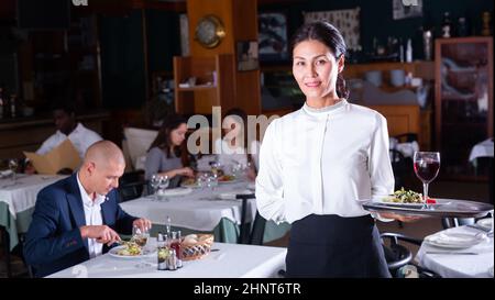 Une serveuse polie avec un plateau de service chaleureux et accueillant au restaurant Banque D'Images