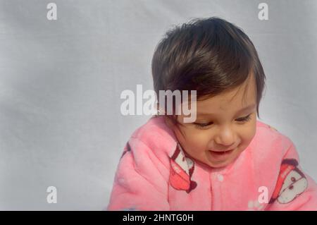 Gros plan Portrait de Happy Baby portant des vêtements chauds en velours rose sur fond blanc. Mignon bébé en combinaison ensemble de mode automne ou hiver lors d'une journée ensoleillée. Petit garçon. Copier l'espace. Vue avant Banque D'Images