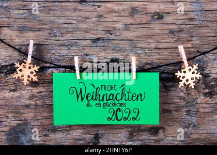 Label vert avec la calligraphie allemande Frohe Weihnachten und Ein Glueckliches 2022 signifie Joyeux Noël et heureux 2022. Corde avec ornamen de Noël. RUS Banque D'Images
