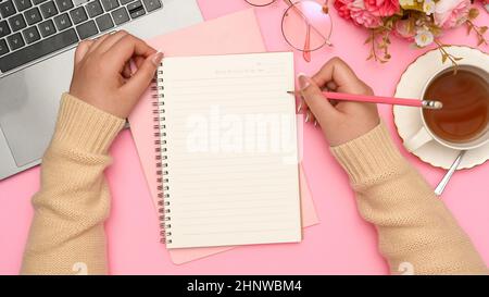 Une étudiante fait ses devoirs, écrit un essai sur son carnet d'école dans son beau bureau rose. Vue du dessus, mains de focus Banque D'Images