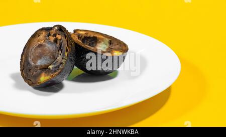 Un avocat coupé en moitié moldy sur une plaque fond jaune Rotten alimentaire contaminé Avocado Necomestibile fruits gâchant nourriture malsaine fruits tropicaux Banque D'Images