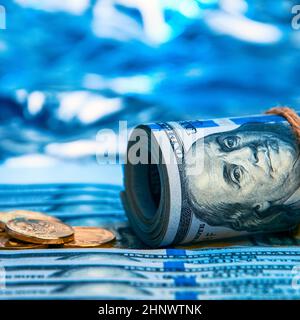 Dollars. Un rouleau de billets de cent dollars et de pièces d'or dispersées sur les billets sur un fond bleu avec un côté. Style bleu. Banque D'Images