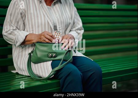 Granny prend les pilules de son sac sur le banc dans le parc d'été. Style de vie des personnes âgées. Jolie grand-mère ayant du plaisir à l'extérieur, vieille femme sur Banque D'Images