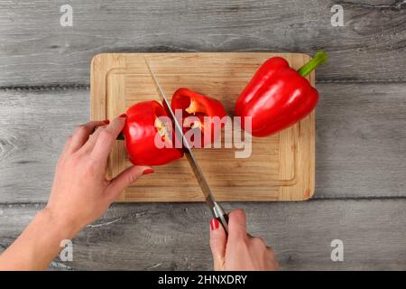 Vue de dessus de table - femme mains tenant le couteau de coupe, chefs de poivron rouge sur la planche à découper. Banque D'Images