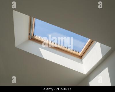 fenêtre en bois dormer dans le plafond blanc en pente donnant sur le ciel bleu Banque D'Images